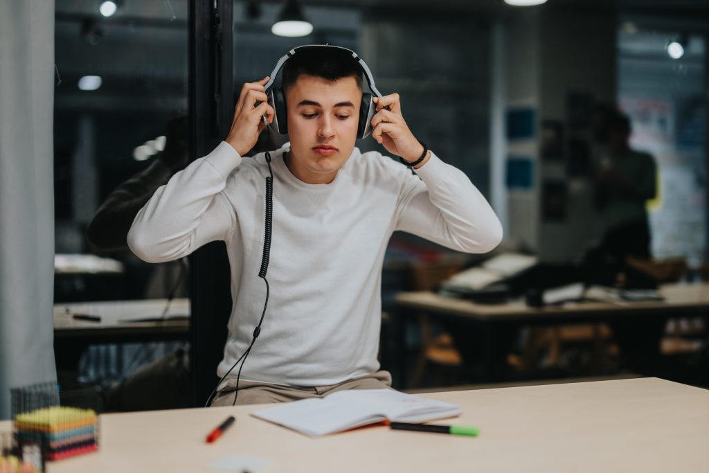 A young student wearing headphones sits at a desk with an open notebook, focused on studying in a classroom setting.