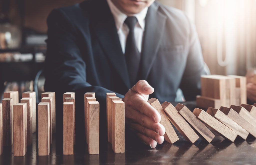 A man in a business suit holds out his hand to stop wooden dominos from collapsing.