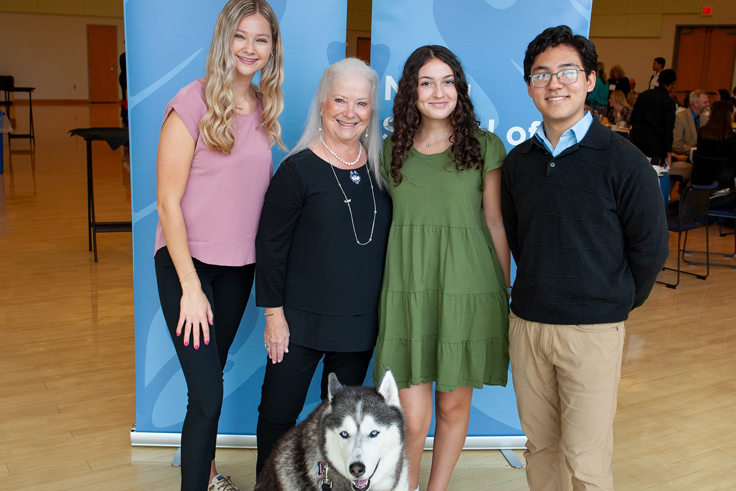 Alum Carla Klein stands with three college students and Jonathan the Husky.