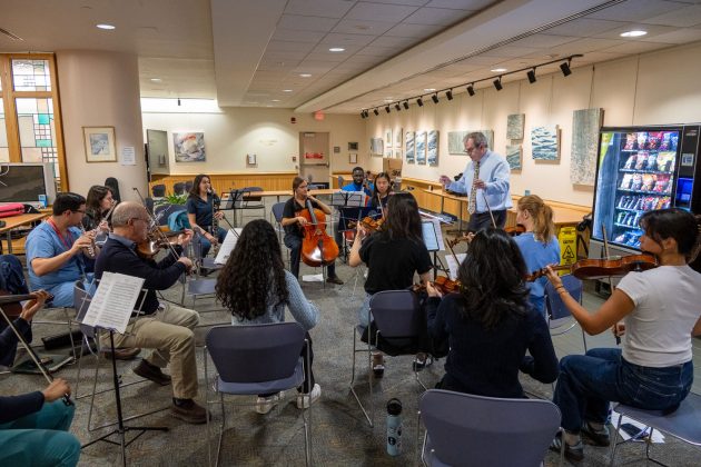 conductor leads string and wind instrumentalists in rehearsal in cafeteria