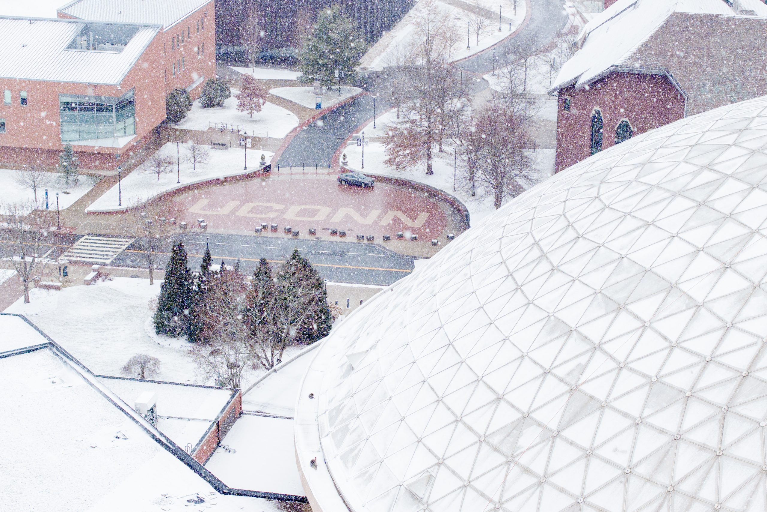 A snow-covered domed building with the UConn logo in bricks in the background