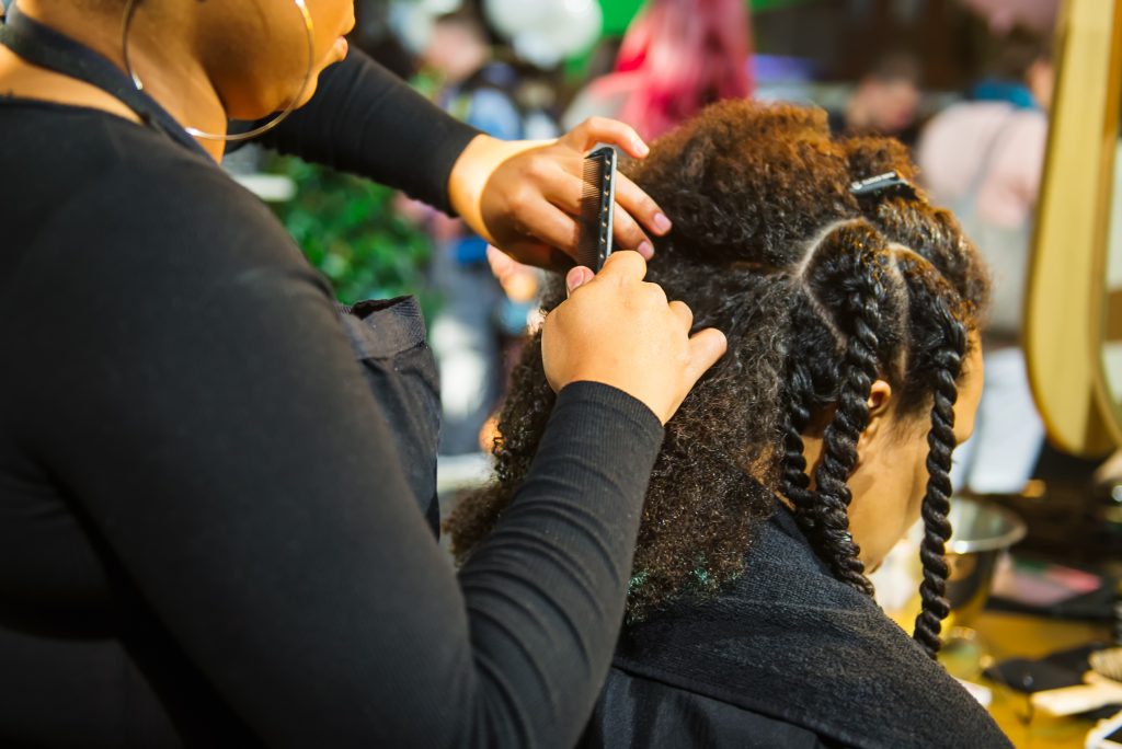 Close up african hairstylist braided hair of afro american female client in the barber salon