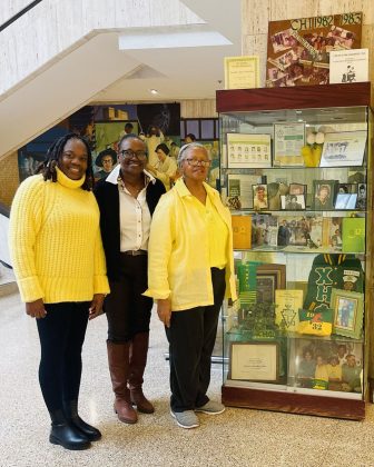 Three women standing beside a Black History Month display