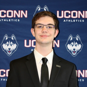 UConn student Greg Bliss stands before a backdrop with UConn logos.