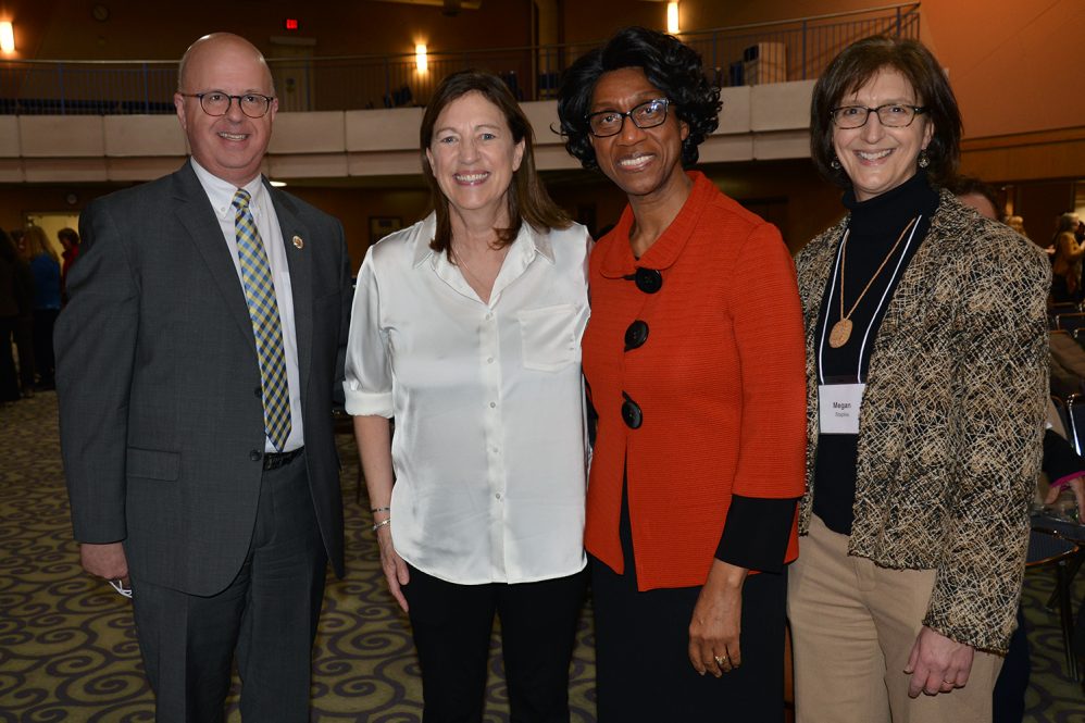 One man and three women pose in a group.