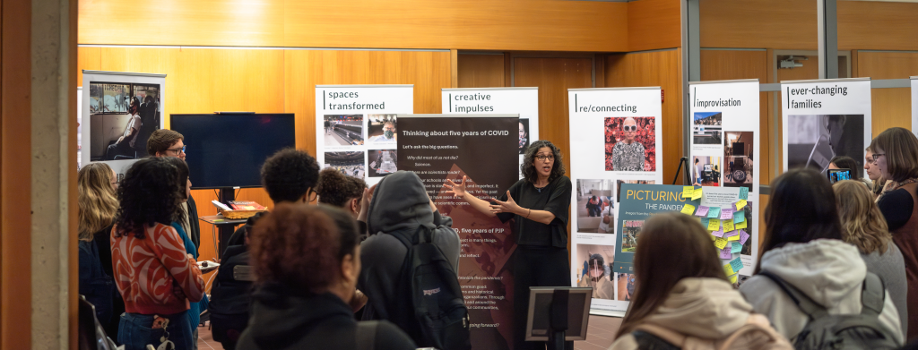 A faculty member in front of a group of people at Homer Babbidge library explains the new exhibit behind her.