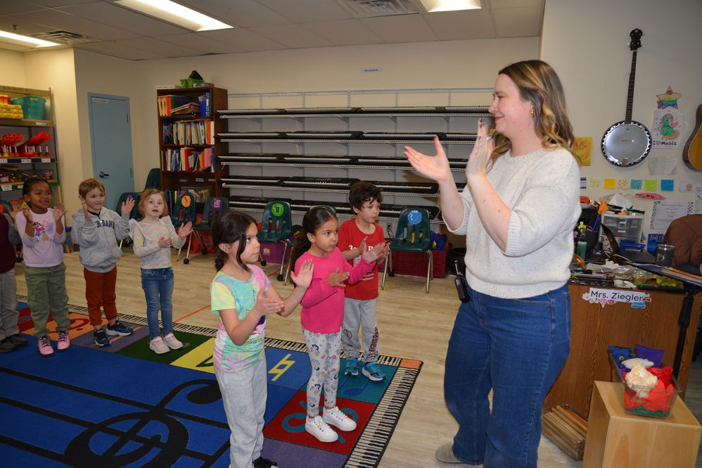 Female educator, Giselle Ziegler, leads a group of kindergarten students in a music class.