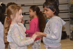 Two kindergarten students hold hands during a music class.