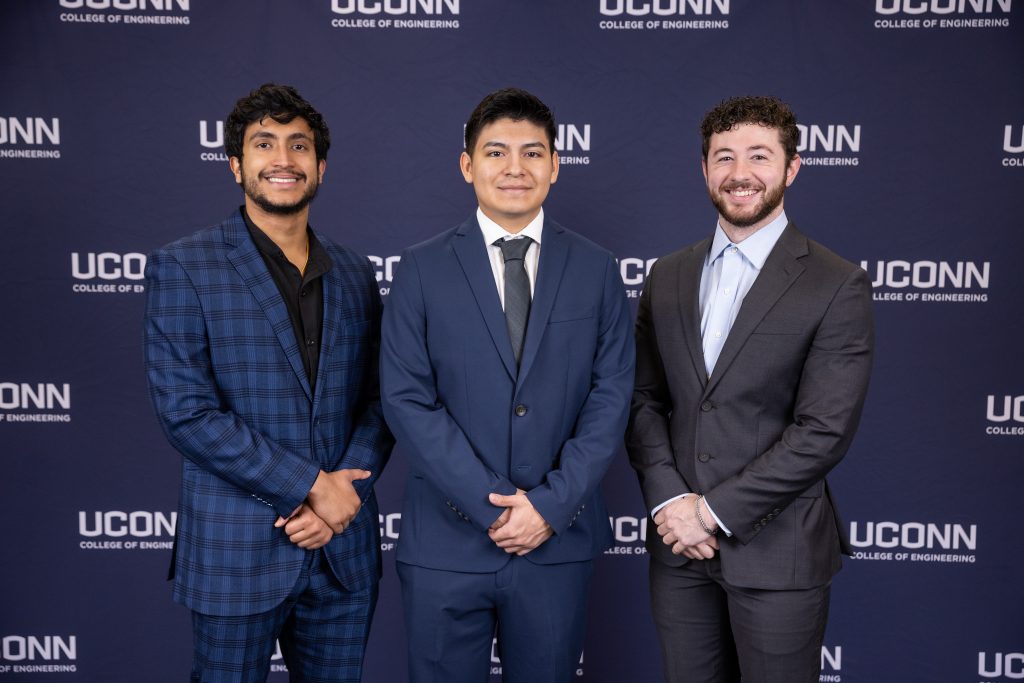 Three male students in suits in front of a UConn College of Engineering backdrop.