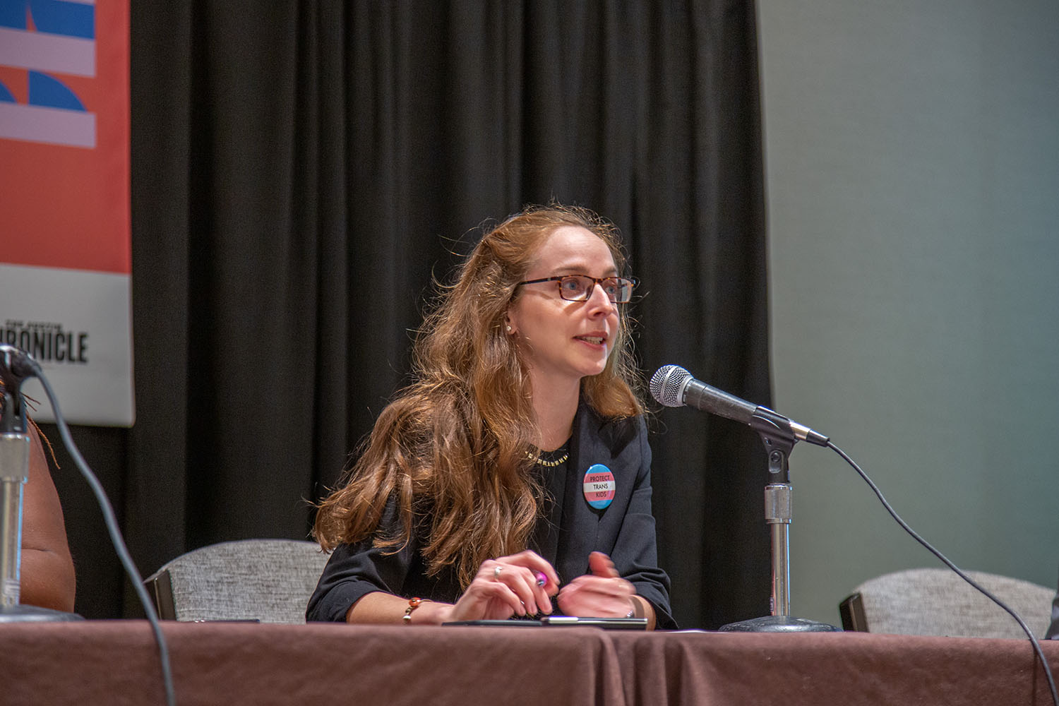 Risa Isard sits at a panel table, speaking into a microphone.