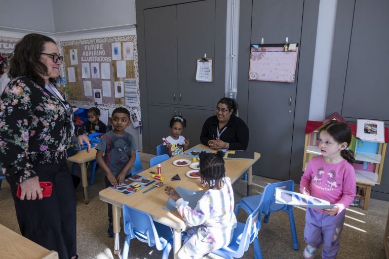 young students gathered around a table with a woman sitting next to them and another woman standing.