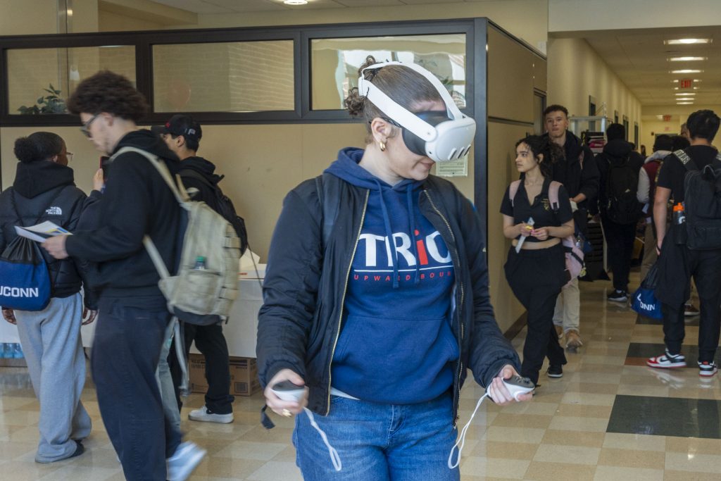 A female student in blue jeans and a blue sweatshirt wears a white VR headset.