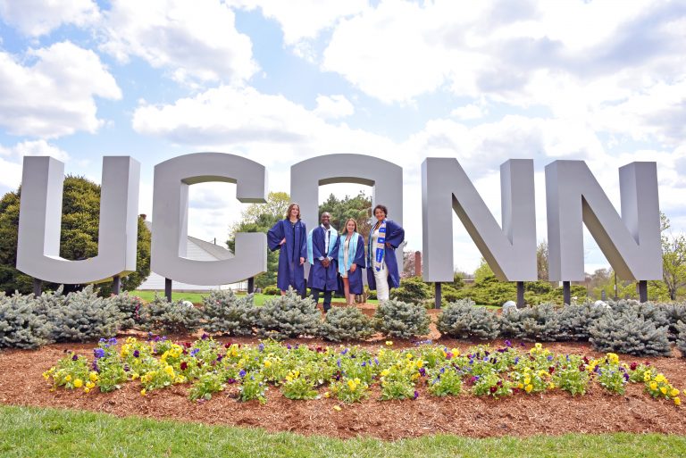 Graduates posing in front of the UConn gateway sign