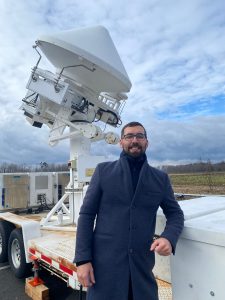 A man in a winter coat stands outside in front of a piece of scientific equipment.