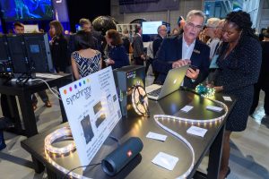 Two people standing in a convention center looking at a strip of LED lights connected to a speaker and computer monitor