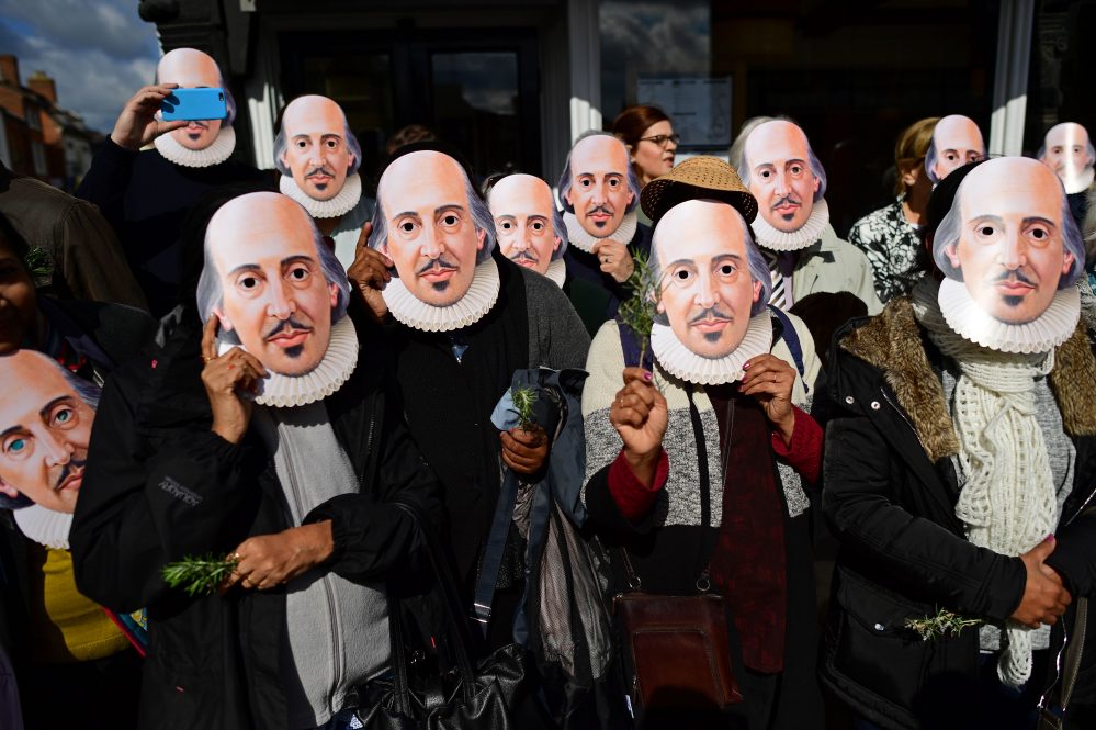 A group of people stand together wearing paper Shakespeare masks.
