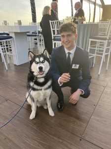 A young man in a blue blazer kneels beside Jonathan XV, UConn's mascot.