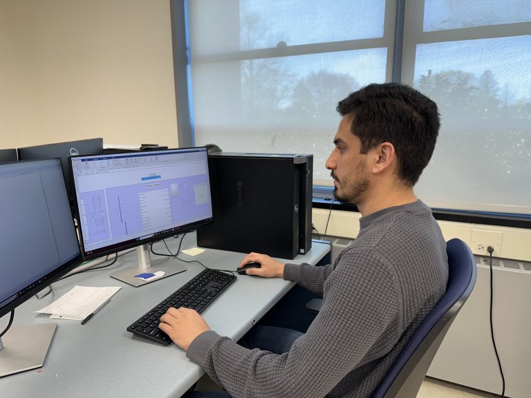 A man working at a desk with two computer monitors, engaged in a task on both screens.
