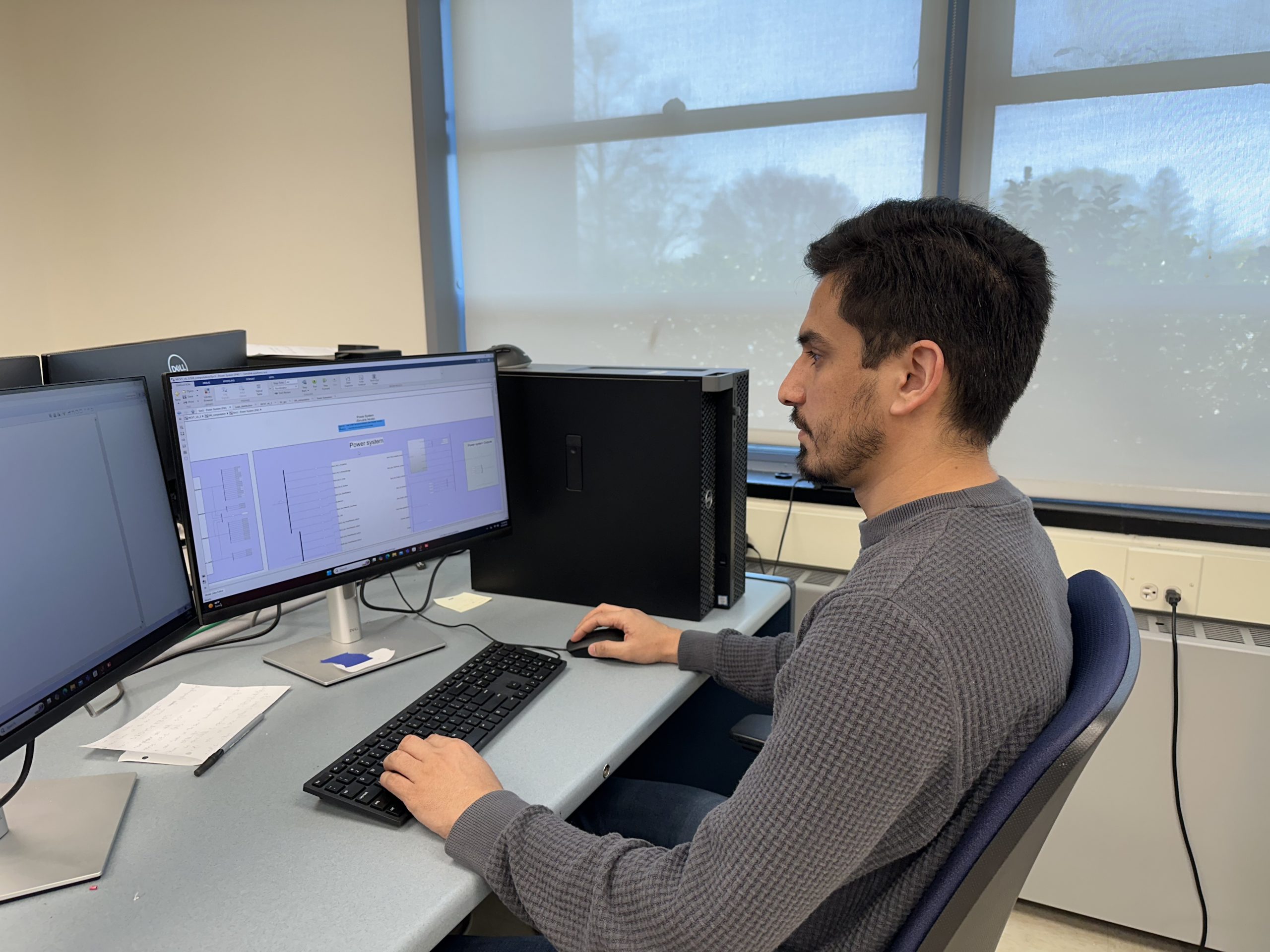 A man working at a desk with two computer monitors, engaged in a task on both screens.