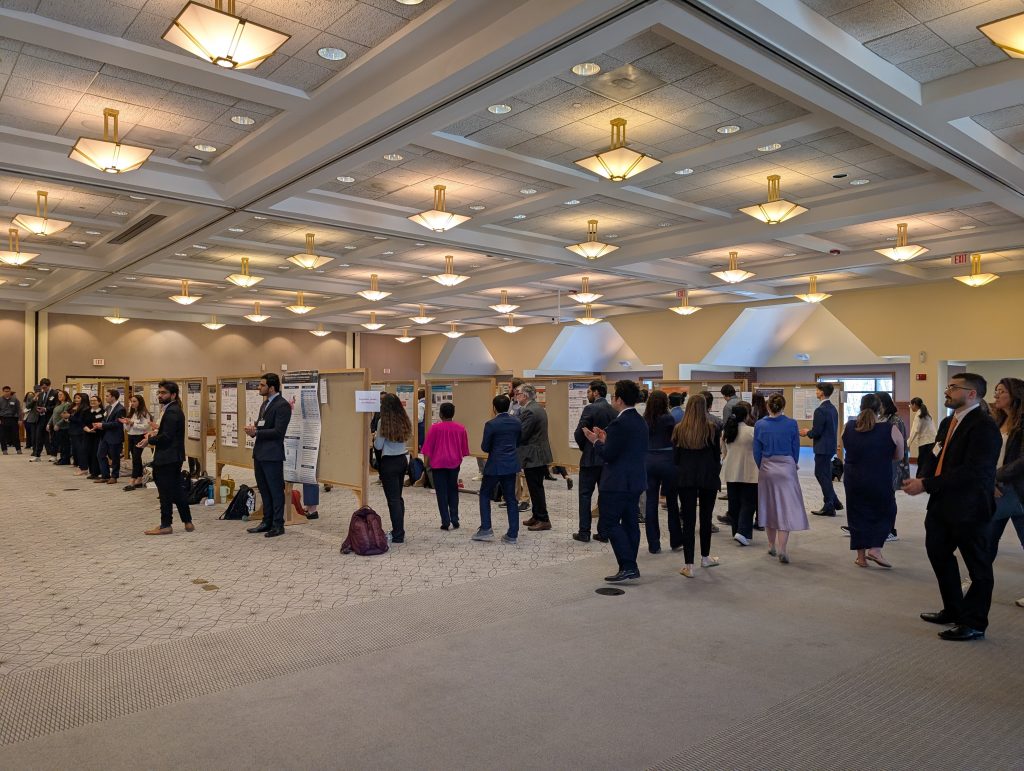 A large group of people standing in a ballroom examine dozens of research posters.