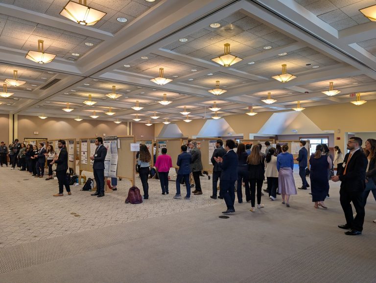 A large group of people standing in a ballroom examine dozens of research posters.