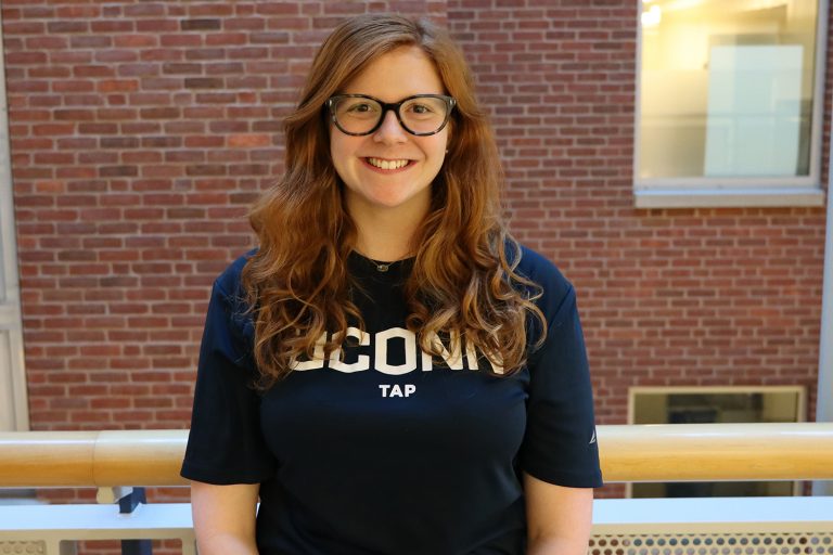 Sara Rosenthal wearing UConn Tap t-shirt stands in the Gentry Building.