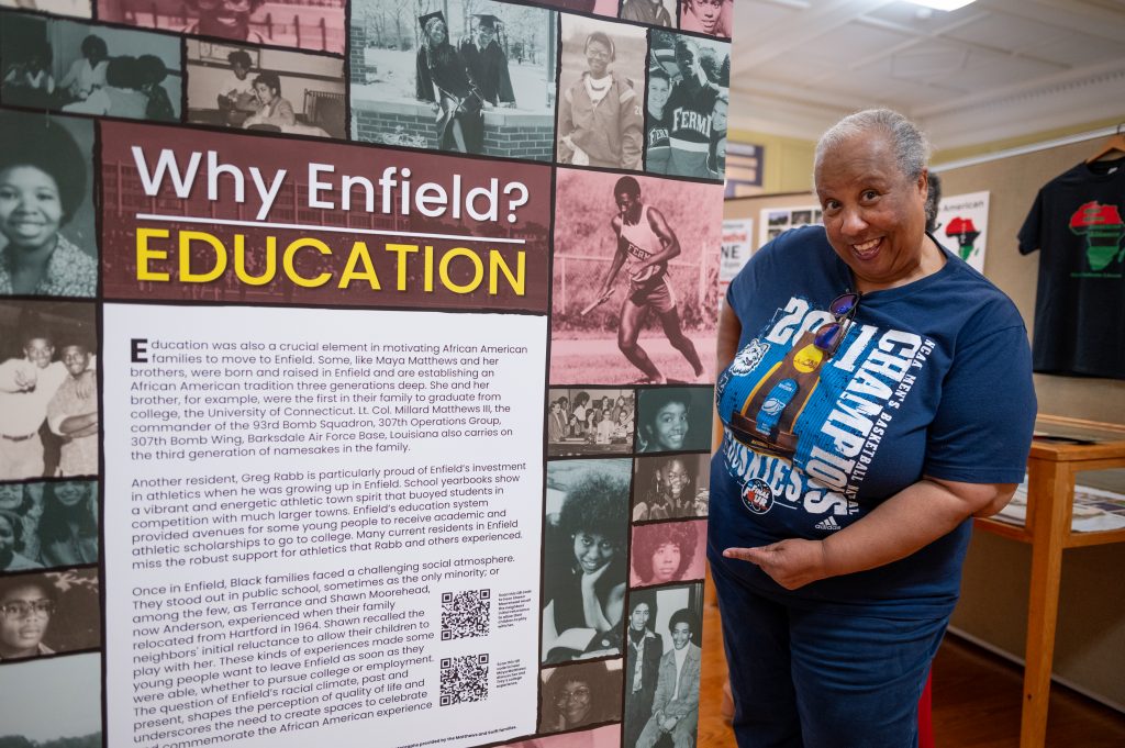 A woman in a blue t-shirt stands next to a history display in Enfield, Connecticut.