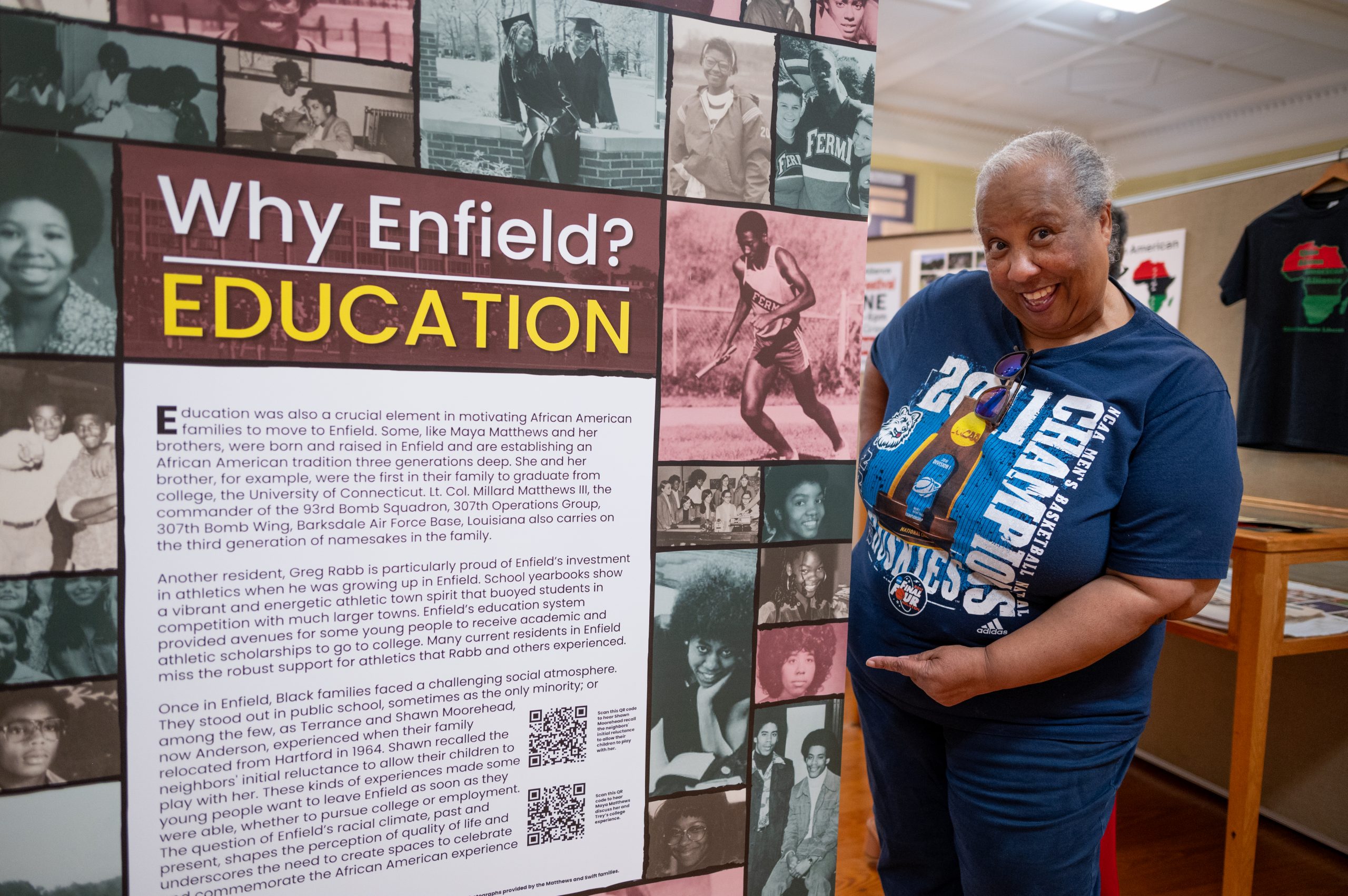 A woman in a blue t-shirt stands next to a history display in Enfield, Connecticut.