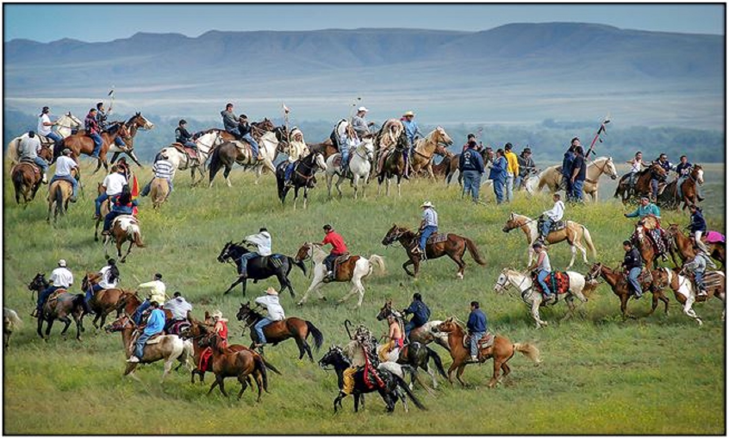 A large number of people on horseback ride with mountains in the background.