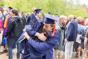 Two people in graduation gowns and caps hug each other.
