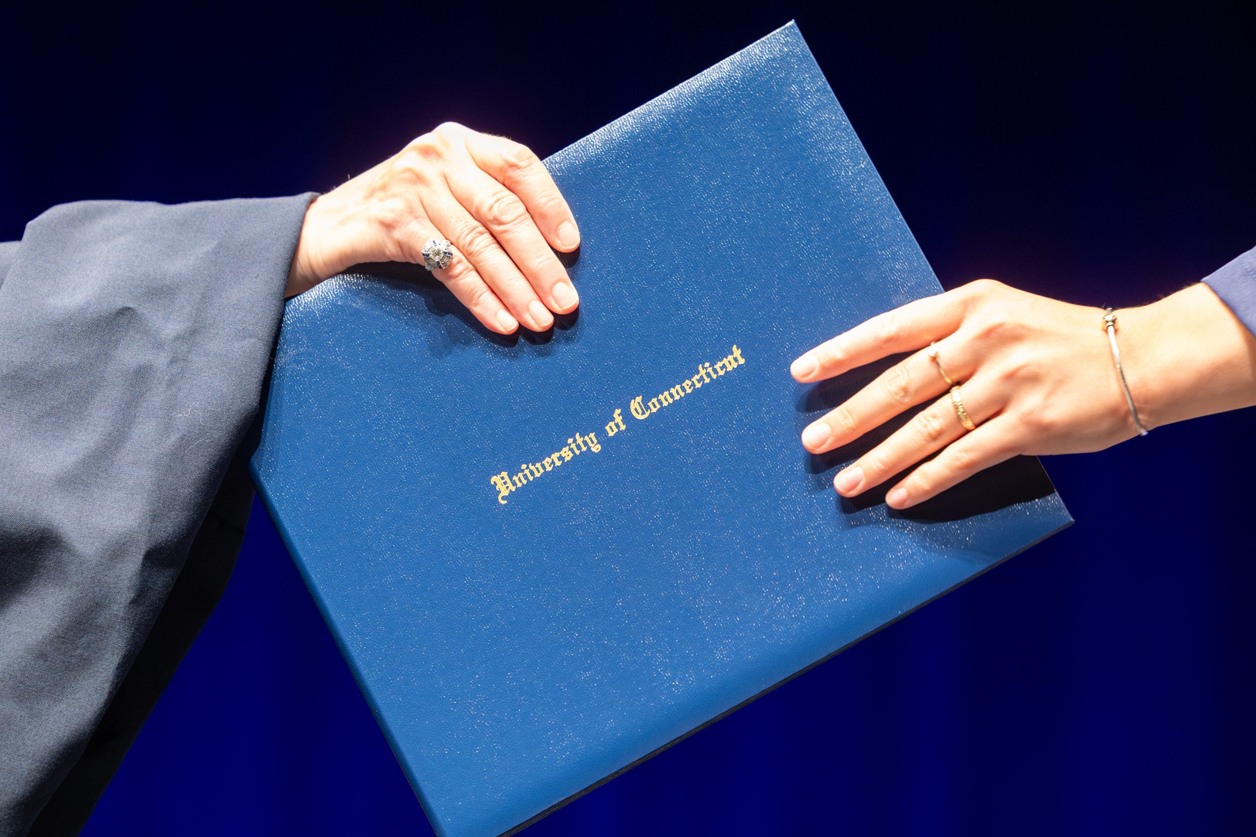 A hand passing off a blue diploma to another hand
