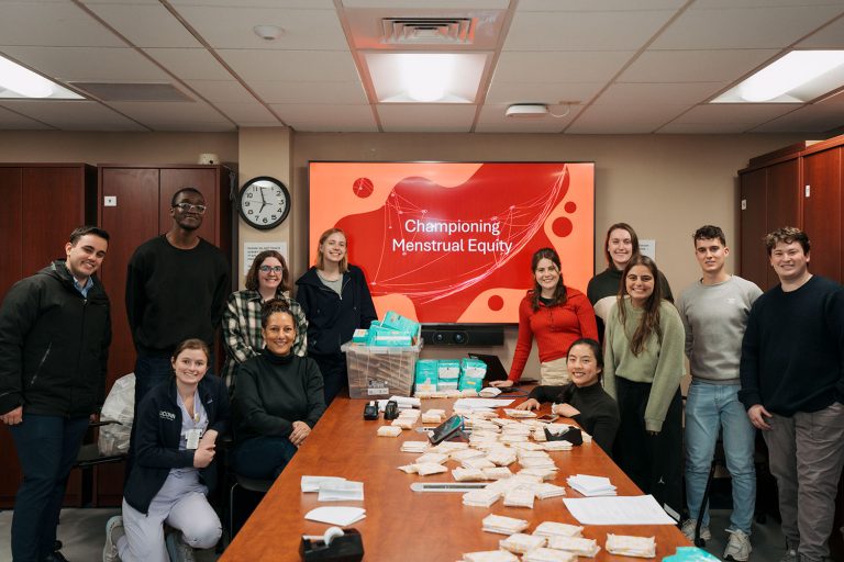 group portrait of 12 in conference room with menstrual products on table in front of 