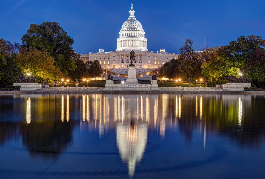 The US Capitol building at night, with the reflecting pool in the foreground.