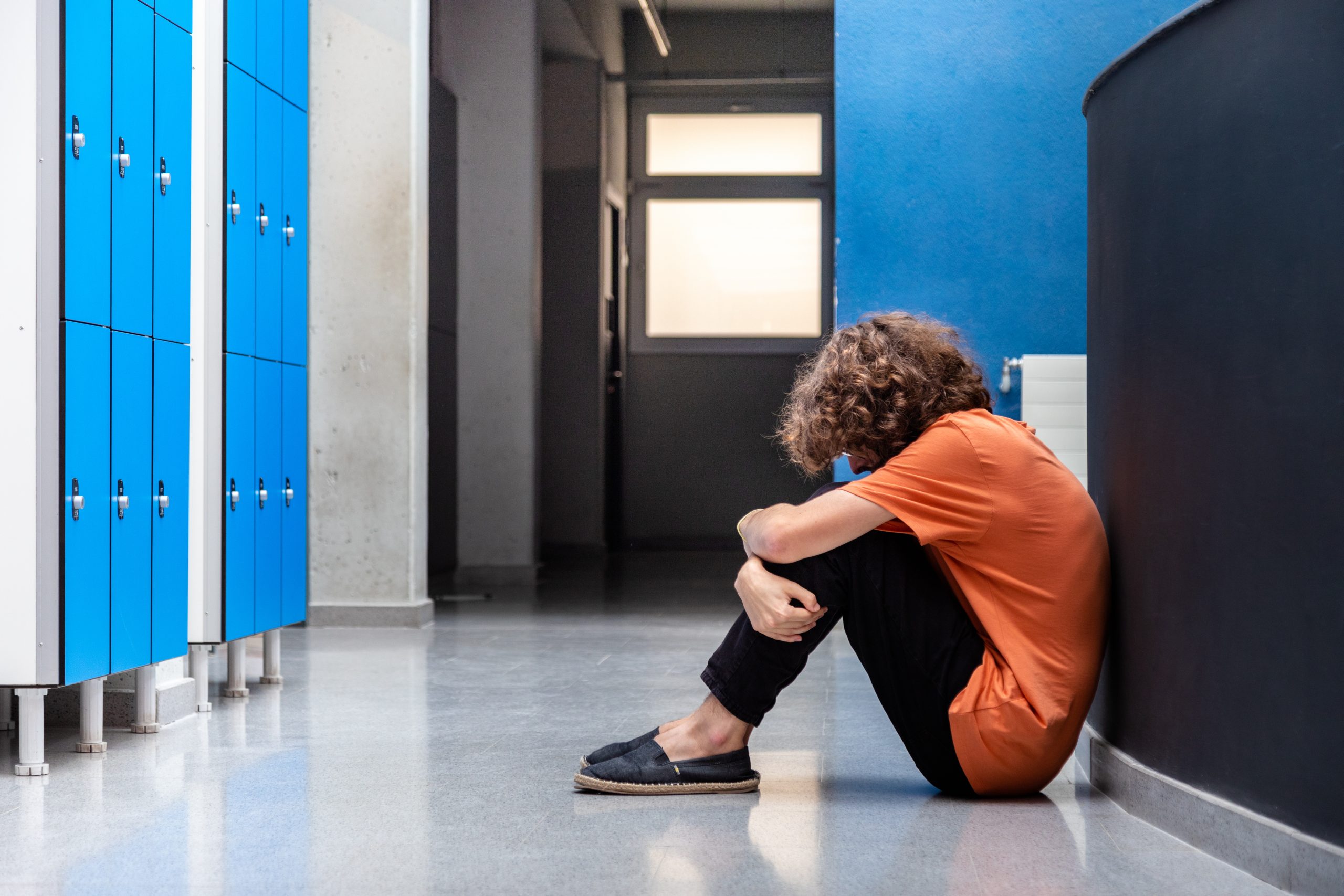 Sad teen boy sitting on floor in high school corridor