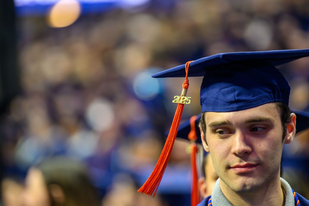 A student's head is in the lower right of the frame, wearing a graduation cap with a tassel that says 2025.