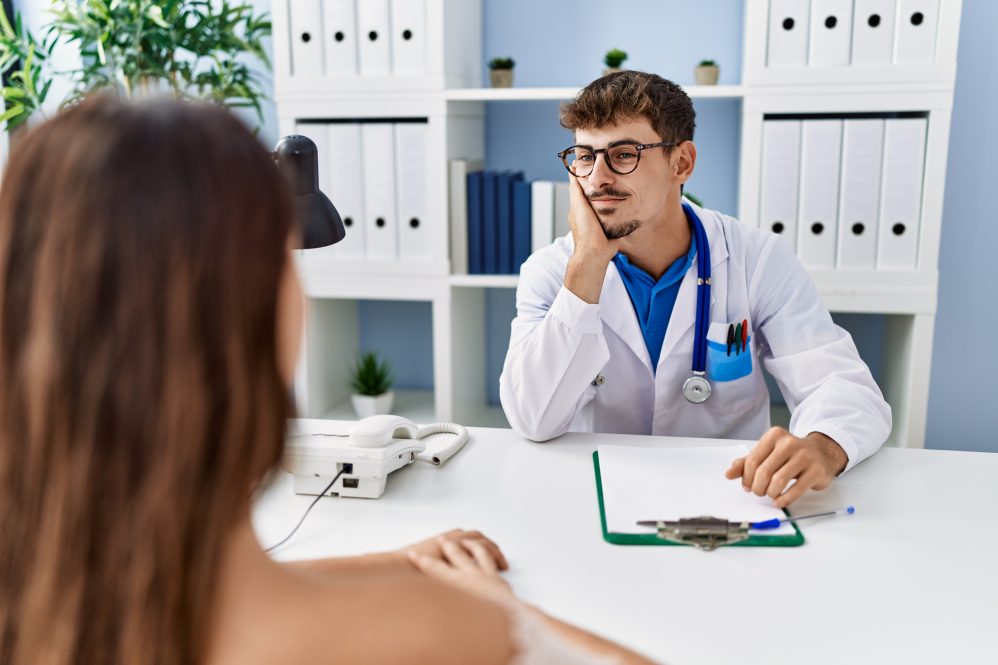 A young doctor looks bored as he listens to a female patient.
