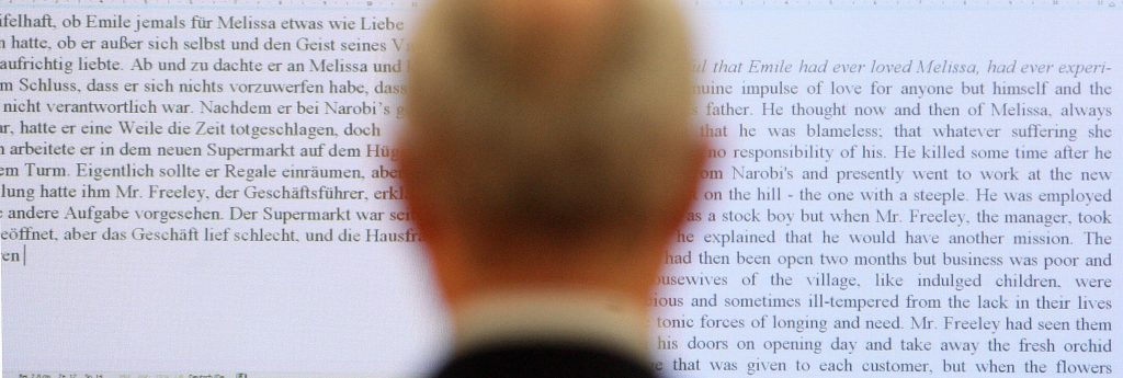 Seen from behind, a man looks at a screen showing the same text in German and English.