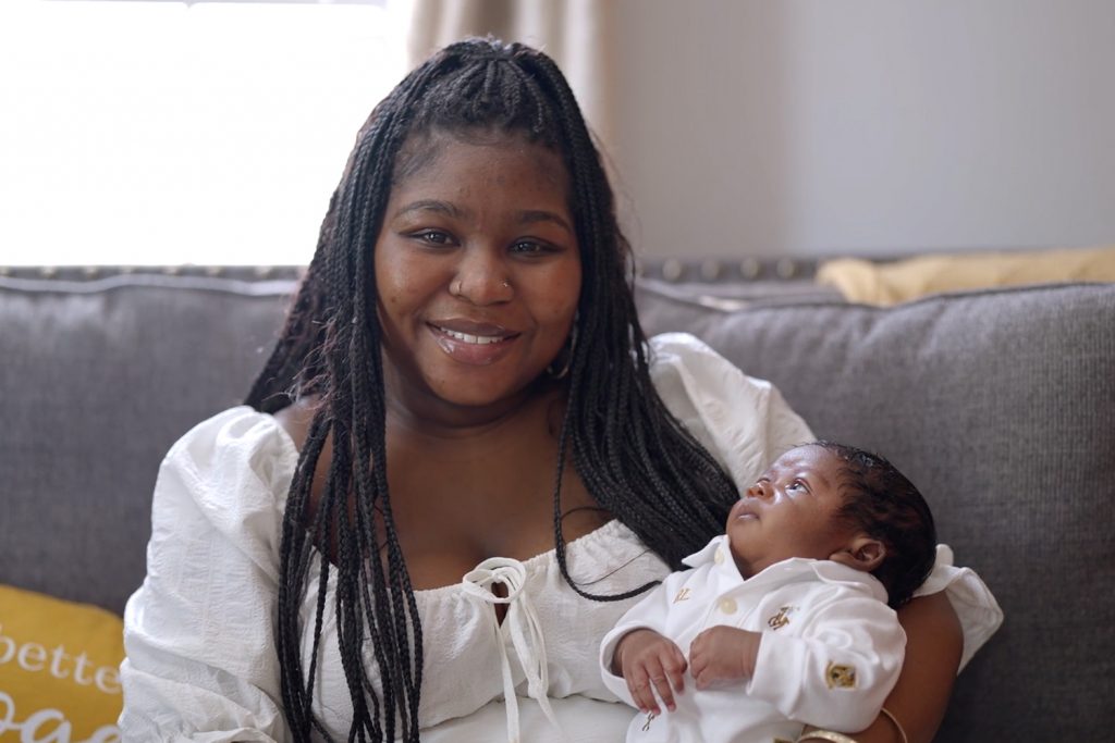 A woman in white sitting holding her newborn son
