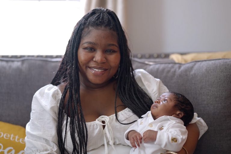 A woman in white sitting holding her newborn son