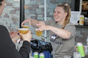 A woman in a grey shirt hands cups of beer to a man.