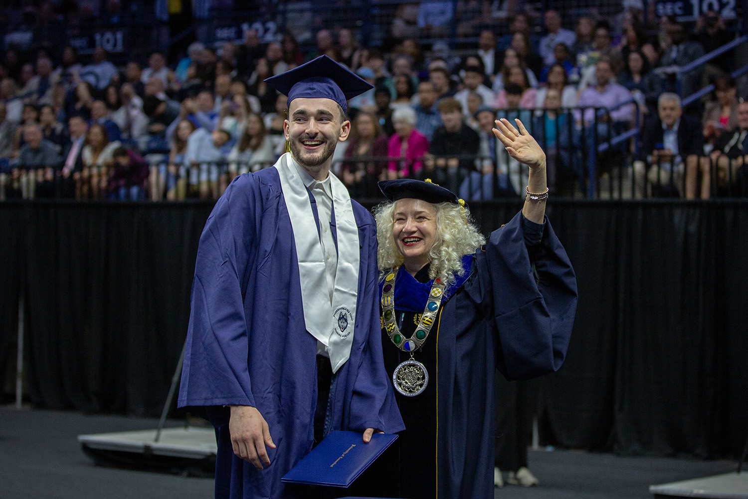 UConn President Radenka Maric waves while standing with Alex Karaban '25 (CLAS) at Gampel Pavilion.