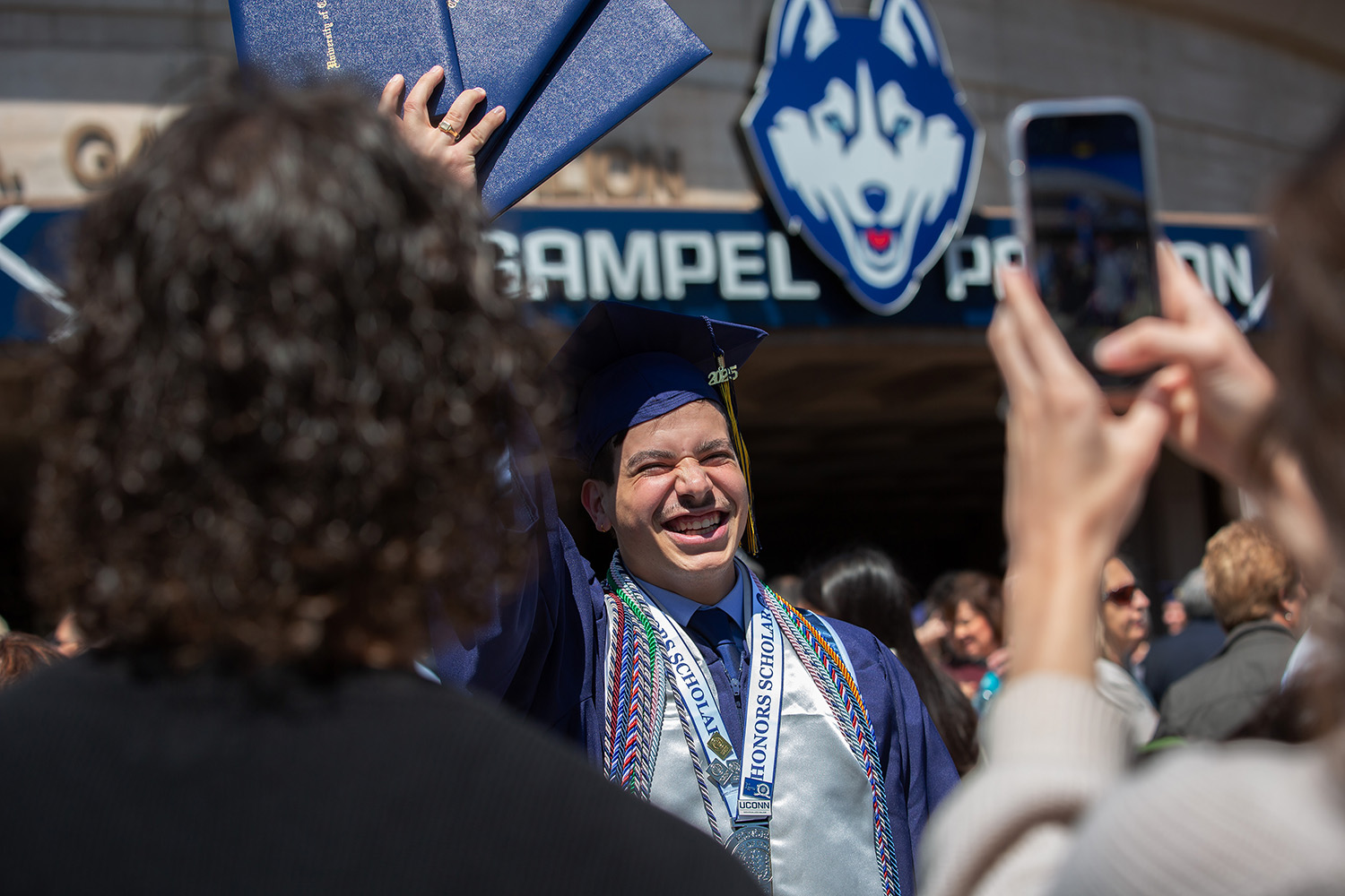 Justin Guinta ’25 (CLAS) holds his diplomas in the air outside Gampel Pavilion.
