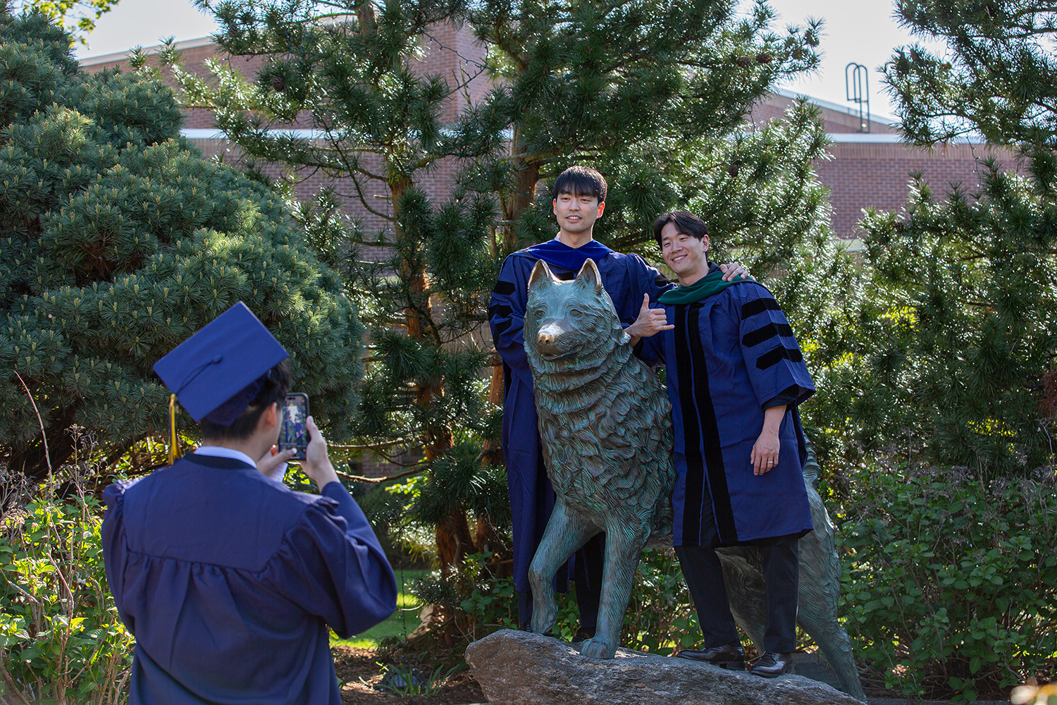 Graduates pose with Jonathan the Husky statue outside Gampel Pavilion.