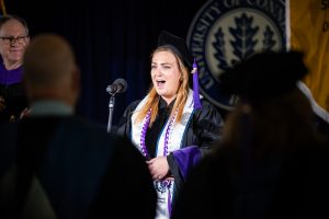 Graduate Bridget Casey sings the national anthem on stage.