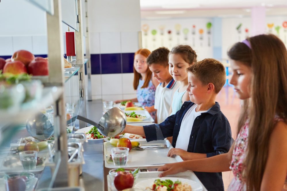 Elementary school students line up in a cafeteria for lunch.