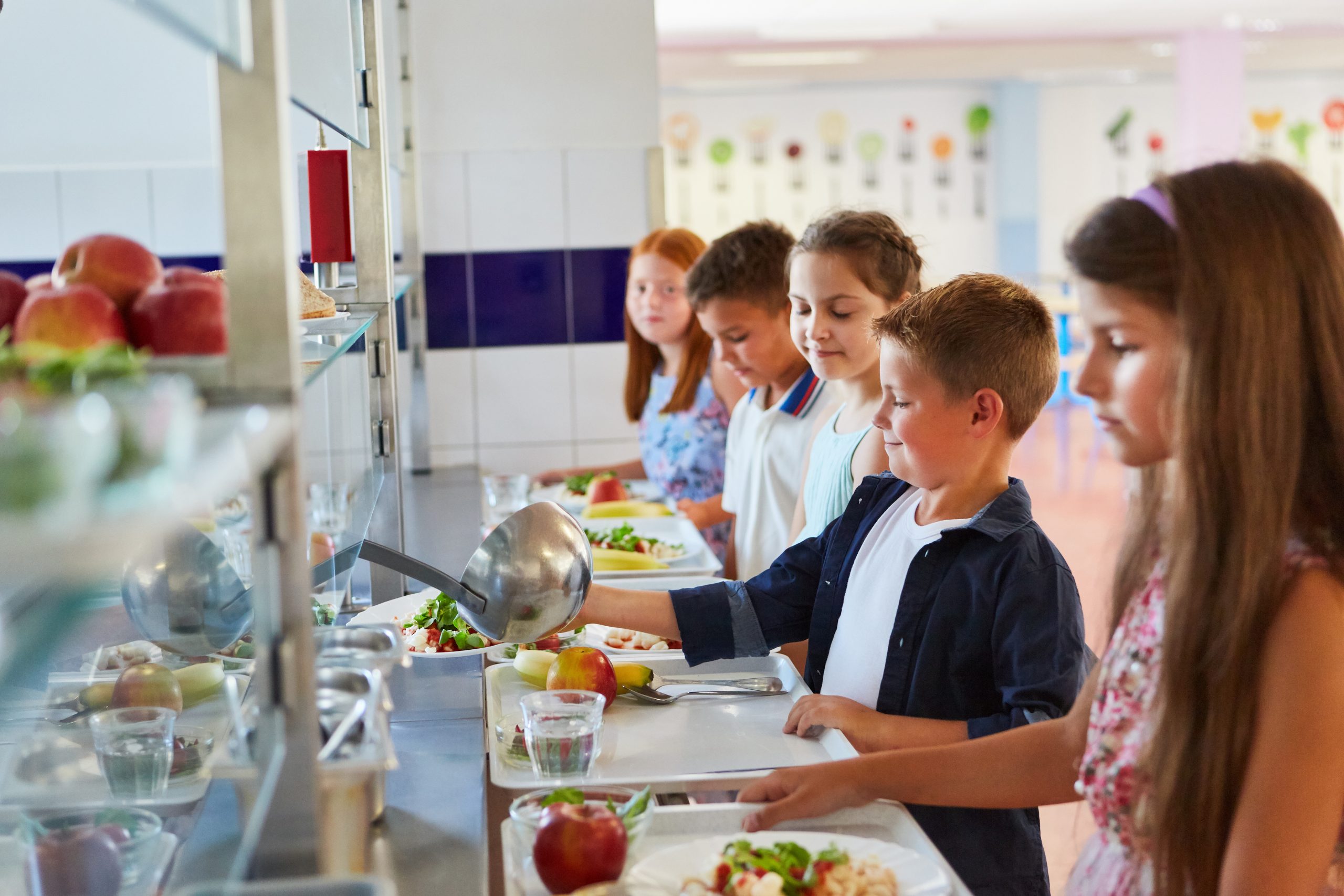 Elementary school students line up in a cafeteria for lunch.