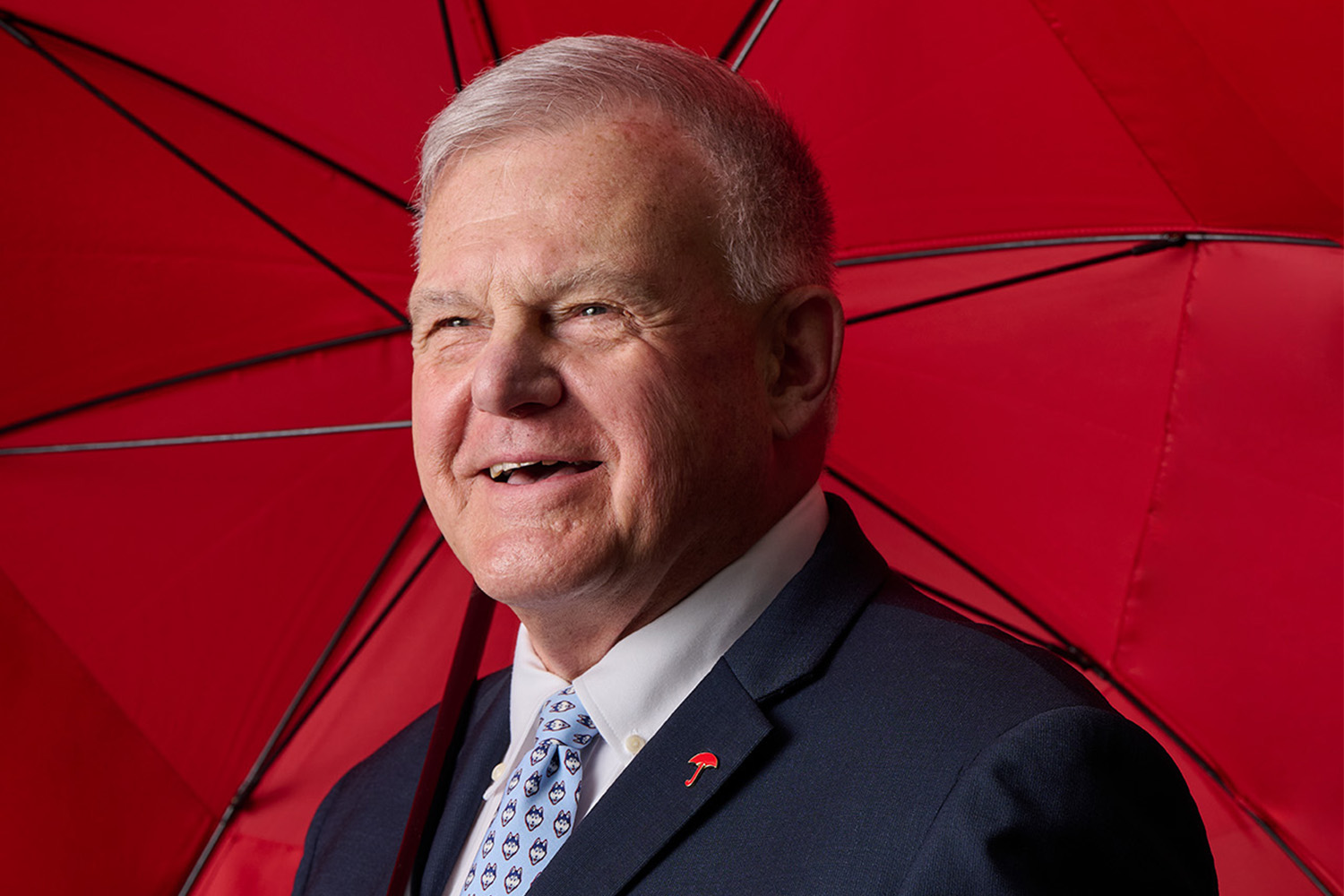 UConn Board of Trustee Andy Bessette posing with a red umbrella behind him
