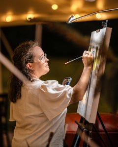 A woman paints on a canvas poised on an easel.