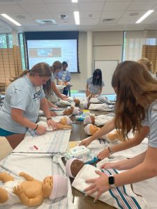 High school students in the Early Introduction to Nursing Profession (EINP) program diapering and swaddling simulation babies on June 26, 2025. (Aime Liggett/UConn Photo)