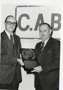 two men holding an award in front of a sign